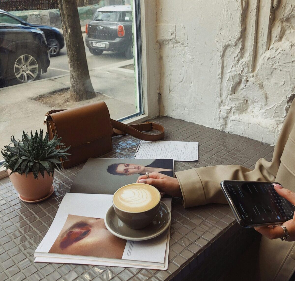 Crop of unrecognizable female tourist in casual wear surfing internet and flipping magazine while drinking coffee in sidewalk cafe