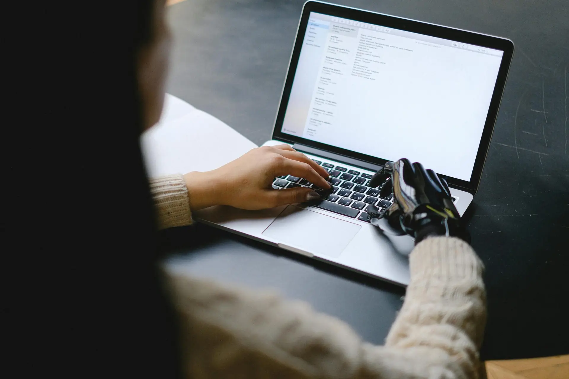 A person with a prosthetic hand using a laptop, showcasing technology and inclusivity.